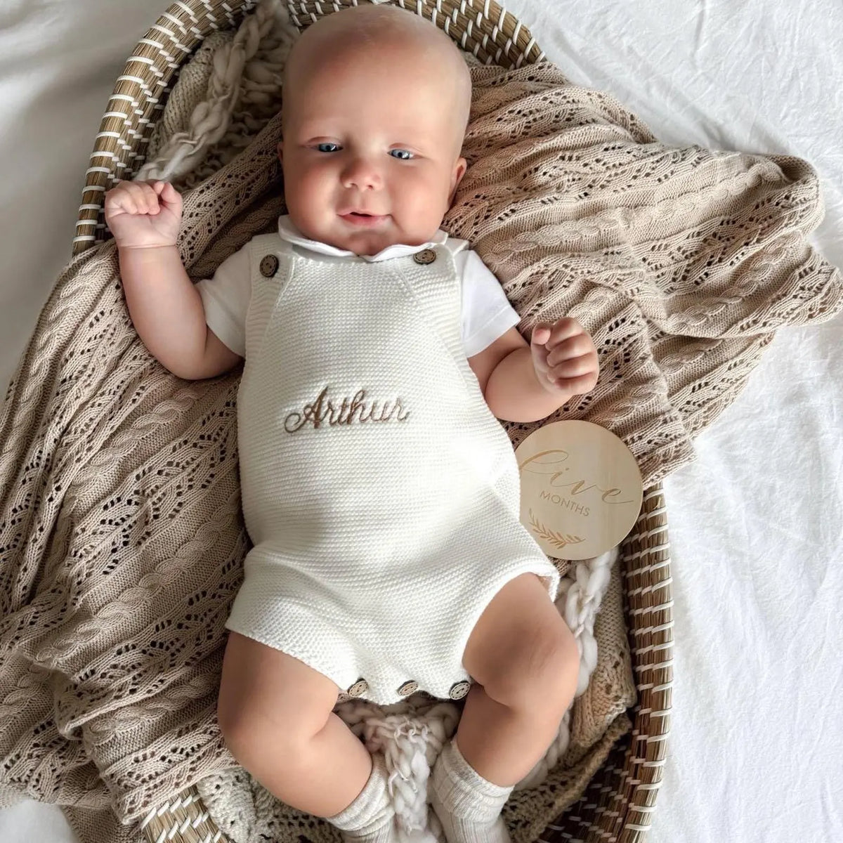 Baby in a white romper with 'Arthur' embroidered, lying on a textured blanket.