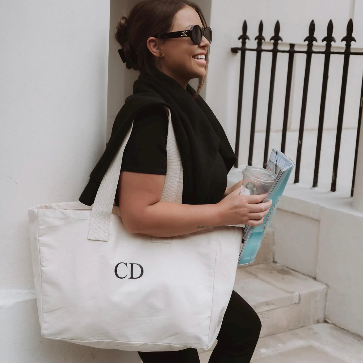 Woman holding a white tote bag with 'CD' initials, standing outdoors.