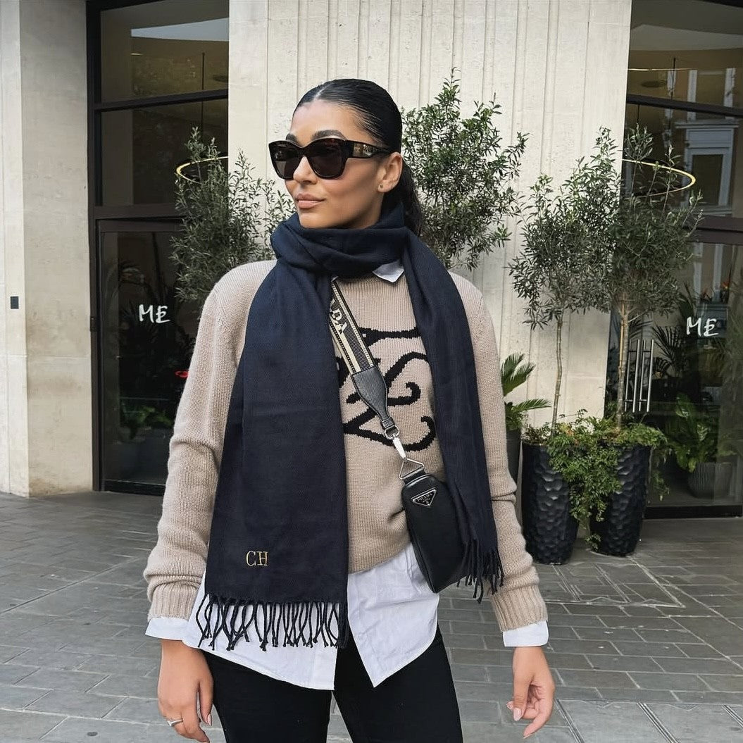 Woman wearing sunglasses, a beige sweater with black patterns, and a dark scarf outdoors.
