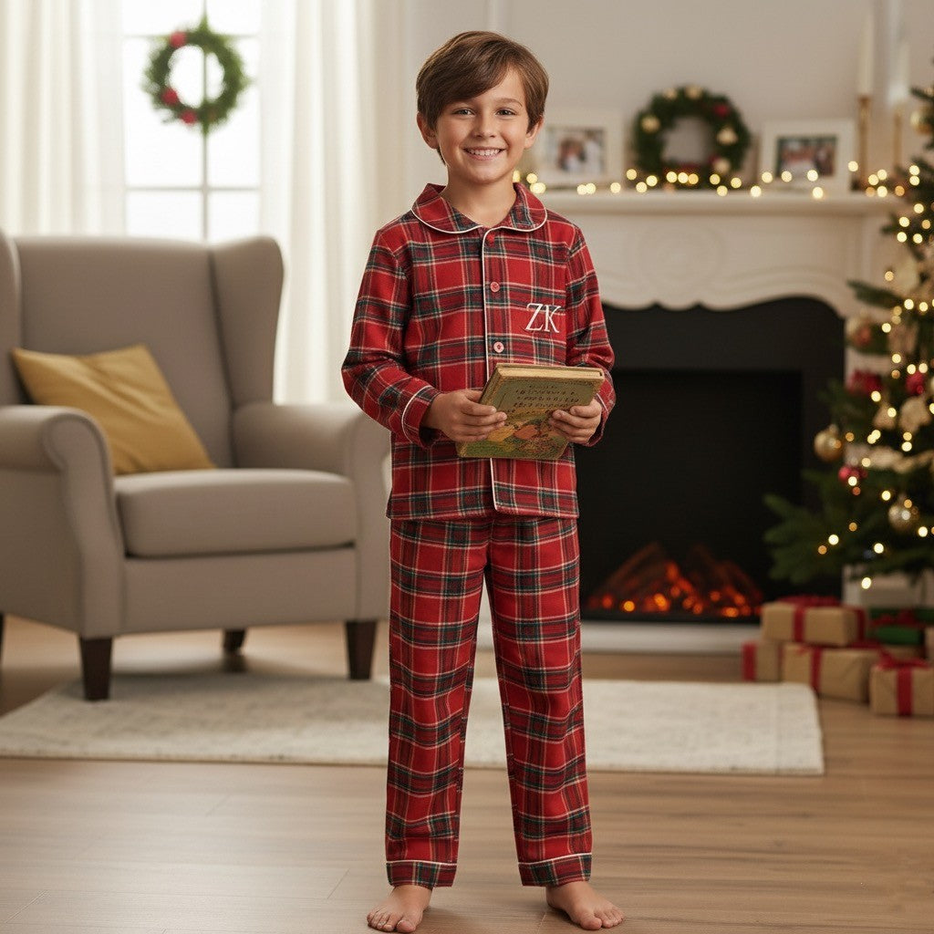 Child in red plaid pajamas holding a book in a festive living room.